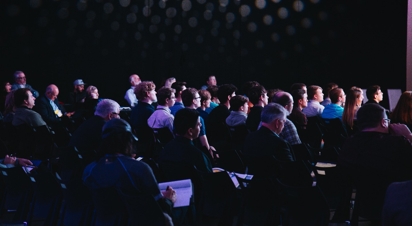 A darkened conference room full of attendees eagerly listening