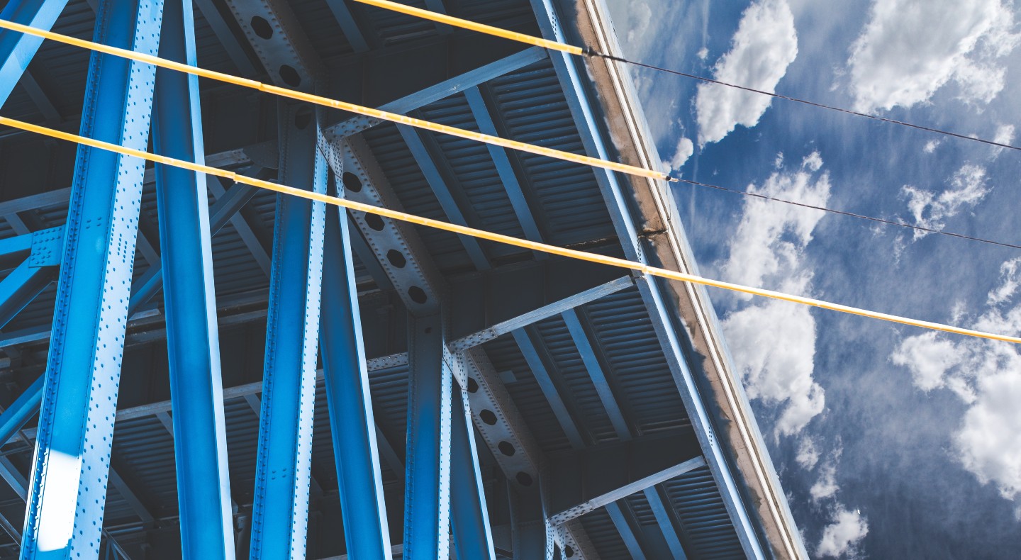 Looking up at a large metal bridge against a cloudy sky